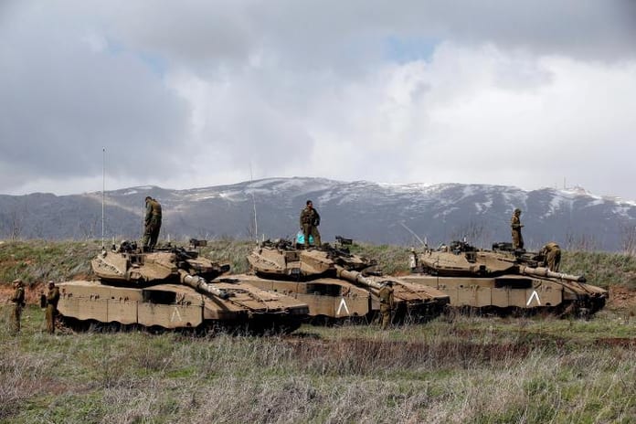 Israeli soldiers stand atop tanks in the Golan Heights near Israel's border with Syria