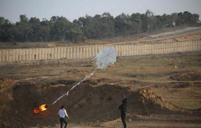 Two-Arab-terrorists-launching-a-firebomb-kite-at-Israel-across-the-Gaza-border-fence-696x445