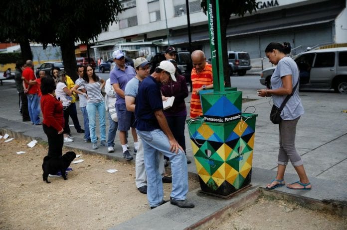 1202071-people-line-up-as-others-charge-their-phones-with-a-solar-panel-at-a-public-square-in-caracas