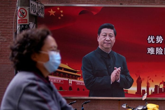 1305112-a-woman-wearing-a-protective-mask-is-seen-past-a-portrait-of-chinese-president-xi-on-a-street-as-the