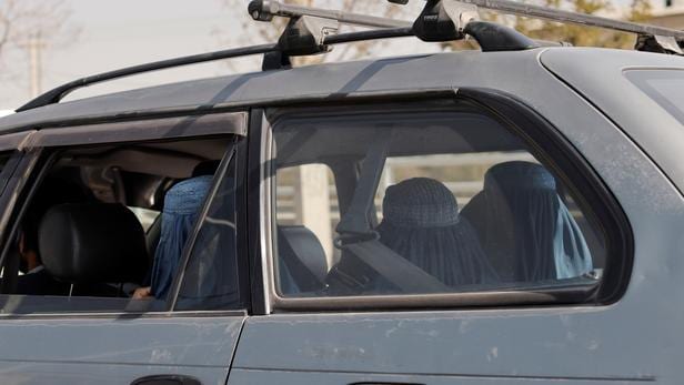 Women wearing burqas sit in the back seat of a car in traffic, in Kabul