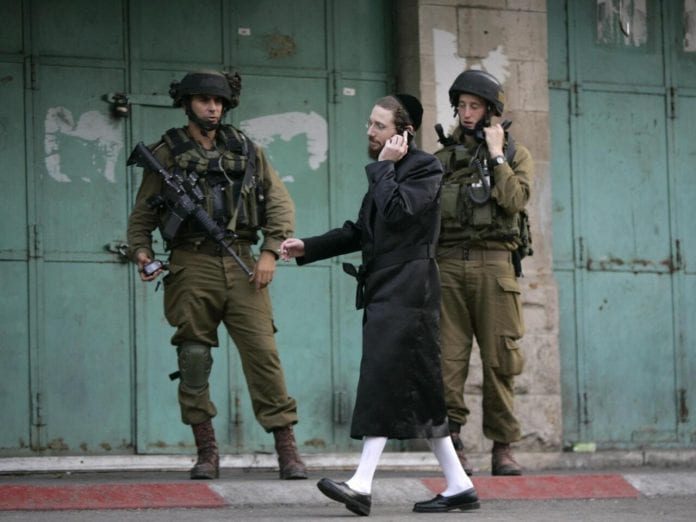 A Jewish worshipper walks past Israeli soldiers standing guard as he makes his way to pray at a site in Hebron