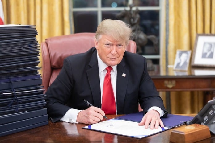 President-Donald-J.-Trump-at-his-desk-in-the-Oval-Office-with-a-stack-of-documents-awaiting-his-signature-December-21-2018.-696x464