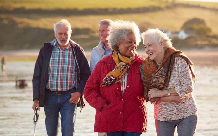 Group Of Smiling Senior Friends Walking Arm In Arm Along Shoreline Of Winter Beach