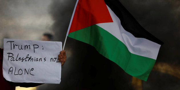 Demonstrator holds a sign and a Palestinian flag during clashes with Israeli troops at a protest near the West Bank city of Nablus