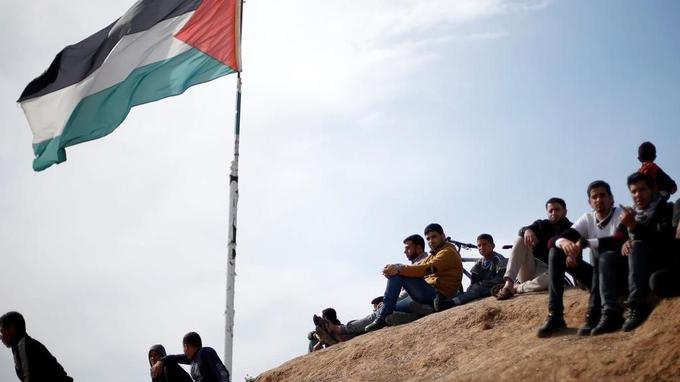 Palestinian sit near to the Israeli-Gaza border fence, ahead of the first anniversary of border protests, east of Gaza City