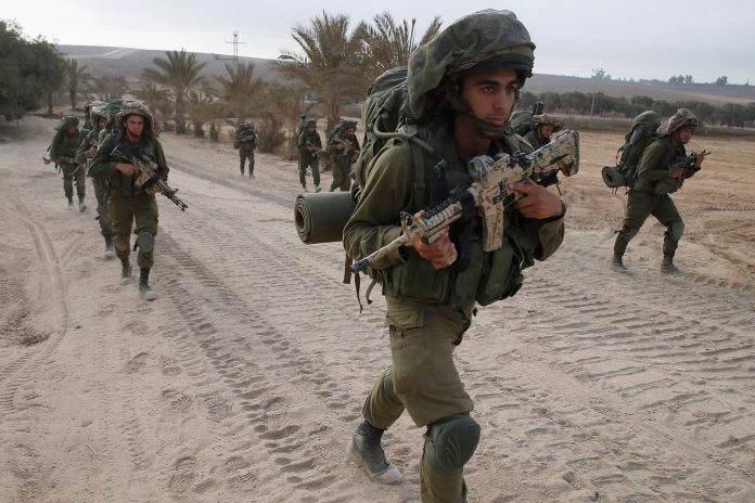 Israeli soldiers walk outside the Gaza Strip as they proceed towards Gaza